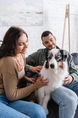 Wall Mural - cheerful young woman cuddling australian shepherd dog near happy boyfriend.