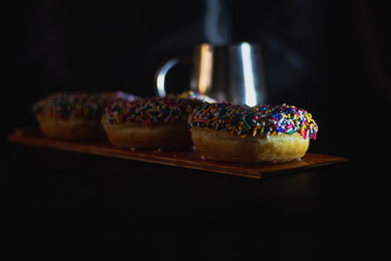 Delicious donuts with sprinkles on a dark background with a mug