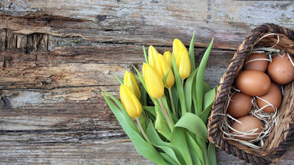 Wall Mural - Background easter. A basket with eggs stands and yellow tulips on a wooden rustic background. Copy space. Flat Lay.