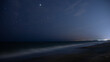 Beautiful view of a blue night sky and stars on dark background over a sandy beach and seawater