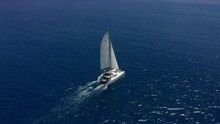 Aerial Footage, Rear View Of Luxury Sailboat Sailing On A Deep Blue Sea With White Wakes. Camera Follow Catamaran In Blue Ocean Water