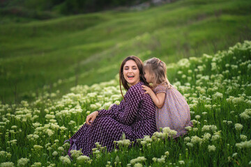 Mom with daughter in park on a green grass during the sunset.