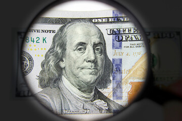 Magnifying glass on the background of a 100 dollars close-up. Zoom to money. Hand holding loupe for dollar inspection.