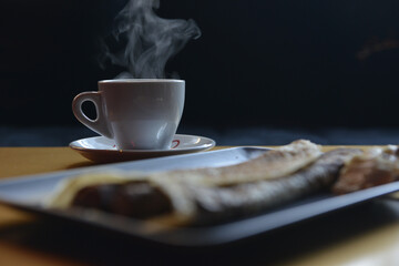 Wall Mural - Selective focus shot of a white mug of hot coffee, and blurred crepes in a pub during snack time