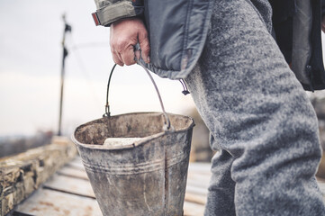 A man carries a metal bucket in his hands filled with parts of the fence, house, walls and ceiling. Establishing order after hostilities on the territory of Ukraine. No war.