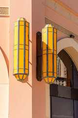 Wall Mural - Close up of two yellow decorated long lamps on the exterior wall on a sunny day in Doha, Qatar