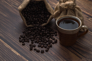 Poster - Closeup shot of a cup of coffee and roasted beans in a burlap sack on wooden surface