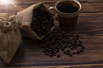 Poster - Closeup shot of a cup of coffee and roasted beans in a burlap sack on wooden surface