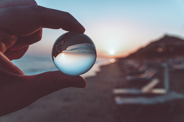 Wall Mural - Close-up shot of person's fingers holding a glass ball reflecting the sunset on it