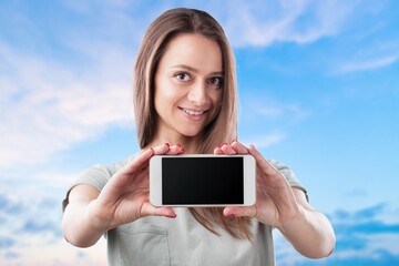 Wall Mural - Smiling beautiful woman wearing T-shirt against blue background  Hold mobile phone with blank empty screen