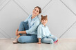 © Pixel-Shot - Portrait of happy mother and daughter sitting on floor near wall