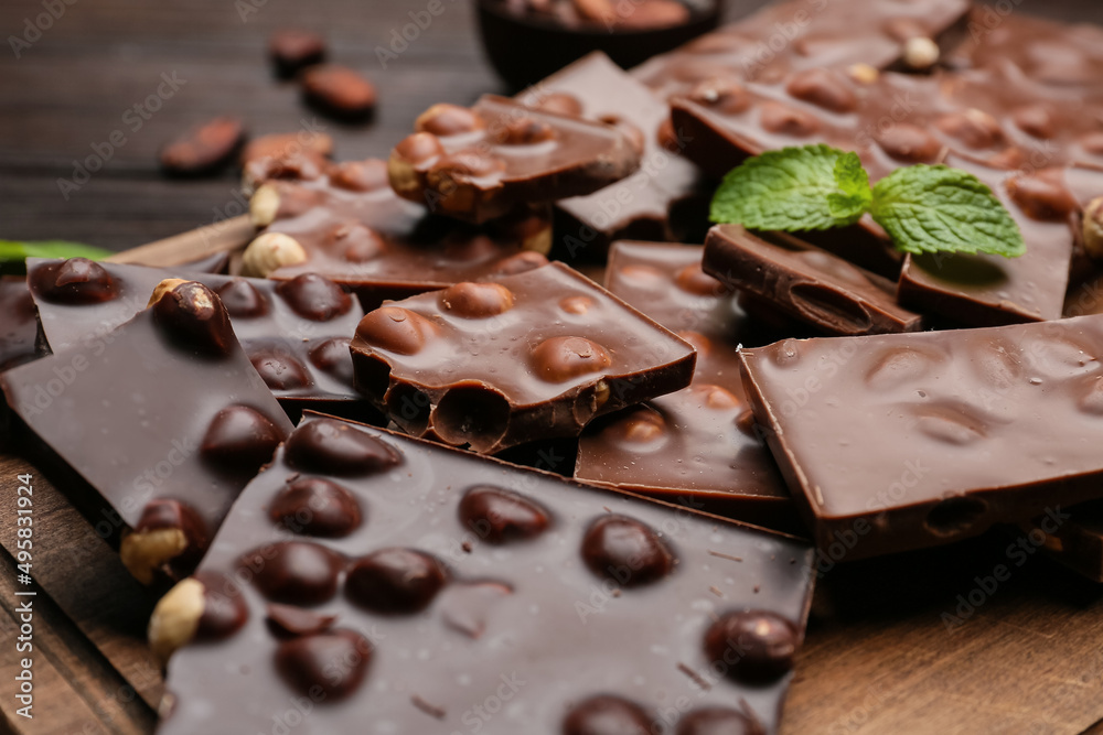 Pieces of tasty chocolate with hazelnuts on board, closeup