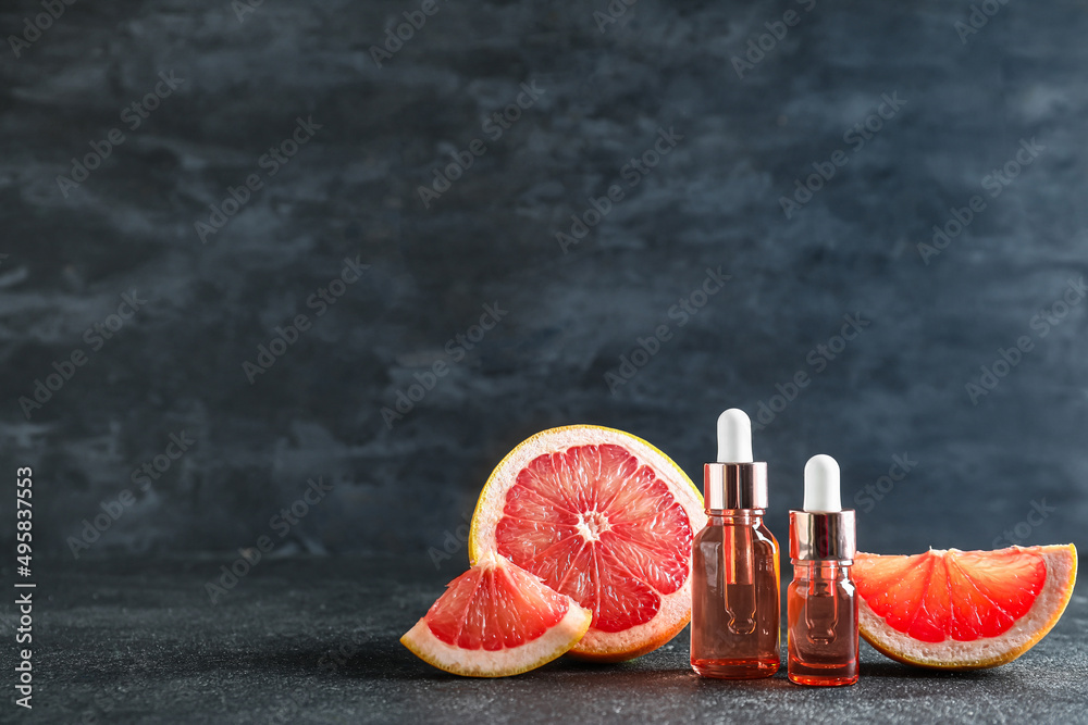 Bottles with essential oil and ripe grapefruit on dark background