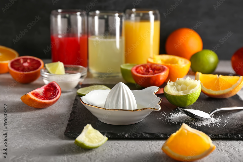 Ceramic juicer, sugar and citrus fruits on grey background