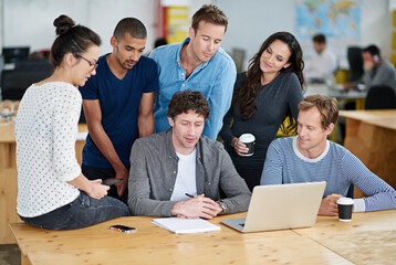 Poster - The merging of creative minds. Shot of a group of colleagues using a laptop together in a casual work environment.