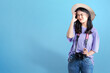 Asian woman with hat and camera standing with unhappy expression