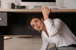 © New Africa - Scared young woman hiding under office desk during earthquake