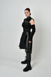 Full length portrait of pretty red haired female model wearing black futuristic scifi leather costume. Dynamic standing poses with gestural hands on a white studio background.