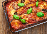 Fototapeta Mapy - Eggplant parmigiana on rustic wooden table. Italian traditional eggplant parmigiana pie with fresh basil and mozzarella cheese. Homemade eggplant parmigiana.