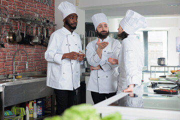 Multiethnic gastronomy experts planning dinner service menu while discussing about what ingredients to use. Professional food industry workers brainstorming lunch meal ideas while standing in kitchen.