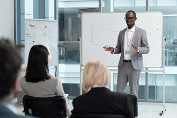 confident teacher in elegant grey suit explaining audience graphic data on whiteboard during lecture