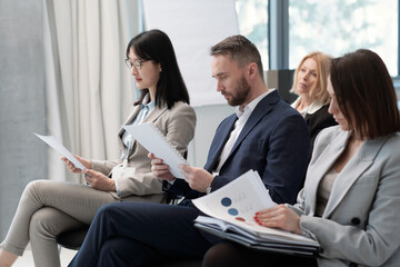 Poster - Group of serious brokers in formalwear looking through their reports at conference in lecture hall while getting ready for speech