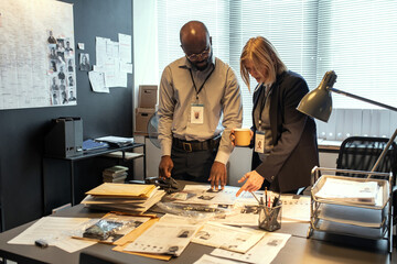 Aufkleber - Two intercultural investigators in formalwear discussing personal information of suspects while female pointing at one of profiles