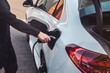 © OrthsMedien - Elektroauto Ladestation, Frau steckt Ladestecker in Ladeeinheit am Fahrzeug