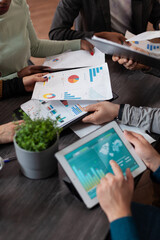 Wall Mural - Closeup of businessman holding tablet computer with marketing graphs on screen. Multiethnic businesspeople working at marketing project sharing papers with company turnover during business meeting