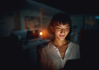 Poster - Never without the latest business news. Shot of a young businesswoman using a digital tablet during a late night at work.
