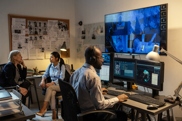 Aufkleber - Young African American FBI agent sitting in front of computer monitors and screen in office while watching security camera records