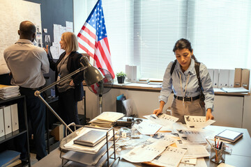 Aufkleber - Young female FBI agent looking through criminal profiles of well-known gang members while her colleagues communicating in front of map