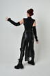 © faestock - Full length portrait of pretty red haired female model wearing black futuristic scifi leather costume. Dynamic standing poses with gestural hands, facing backwards away from  on a white studio backgro