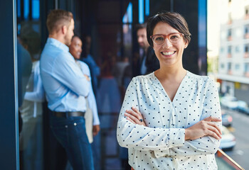 Aufkleber - She loves being a part of the team. Portrait of a young businesswoman standing on a balcony with her arms crossed and her coworkers in the background.