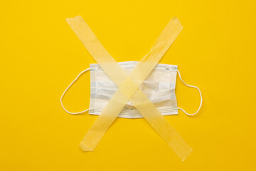 Medicine mask sticked up with masking tape isolated on yellow background with copy space. Concept of pandemic restrictions during covid coronavirus time. Stay safe and care about people health