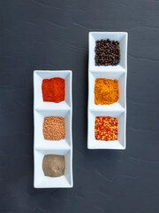 Wall Mural - Flat lay red and black pepper, yellow turmeric root powder and mustard seeds in white bowls on gray table