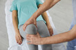 Male therapist massaging knee of female patient during physiotherapy session at the hospital. Close up of woman's knee lying on medical couch. Concept of osteopathy and chiropractic leg adjustment.
