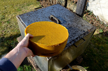 work of a beekeeper melting old dark wax combs full of diseases in a stainless steel steam boiler. big cake of wax on apiary shows beekeeper. It has several kilos for sale, price of beeswax is rising