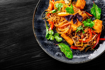 Wall Mural - asian noodles with fried cheese tofu and vegetables in plate on black wooden table background