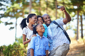 Everybody smile and say nature. Shot of a happy-looking family taking a self portrait with a camera phone while out hiking in the forest.
