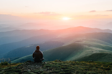 Alone tourist on the edge of the mountain hill against the backdrop of an incredible sunset mountains landscape