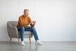 © Prostock-studio - Portrait of mature man using smartphone sitting on armchair