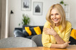 Close-up portrait on blonde-haired woman in home interior. Charming mature caucasian lady looking away and smiles, resting, serene female spending weekend at home