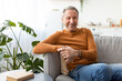 © Prostock-studio - Smiling mature man sitting on the couch and posing