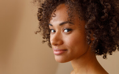 Wall Mural - Attractive woman with curly hairstyle posing against beige wall