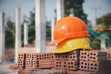 Wall Mural - Safety helmet (hard hat) for engineer, safety officer, or architect, placed on cement floor with brick background. Yellow and Orange safety hat (helmet) in construction site.