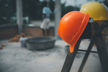 Wall Mural - Safety helmet (hard hat) for engineer, safety officer, or architect, placed on cement floor with brick background. Yellow and Orange safety hat (helmet) in construction site.