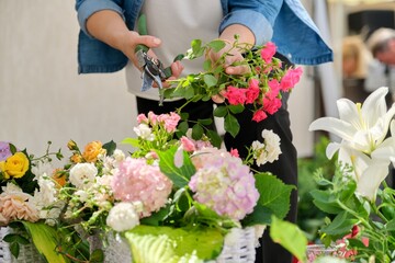 Poster - Woman florist making flower arrangement in basket outdoor.