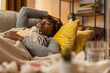 © ABCreative - A dark-skinned woman lies in bed as prescribed by her doctor. The girl has struggled all night with fever and runny nose, she is tired, many medicines and tissues beside her.