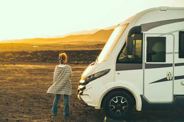 Wall Mural - Concept of travel and freedom. Back view of standing woman admiring desert landscape near modern camper van motorhome. Alternative home lifestyle female people looking sunset free